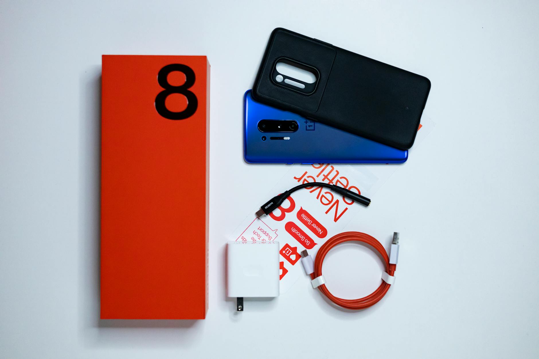 Flat lay photo of OnePlus 8 smartphone unboxing with accessories on a white background.