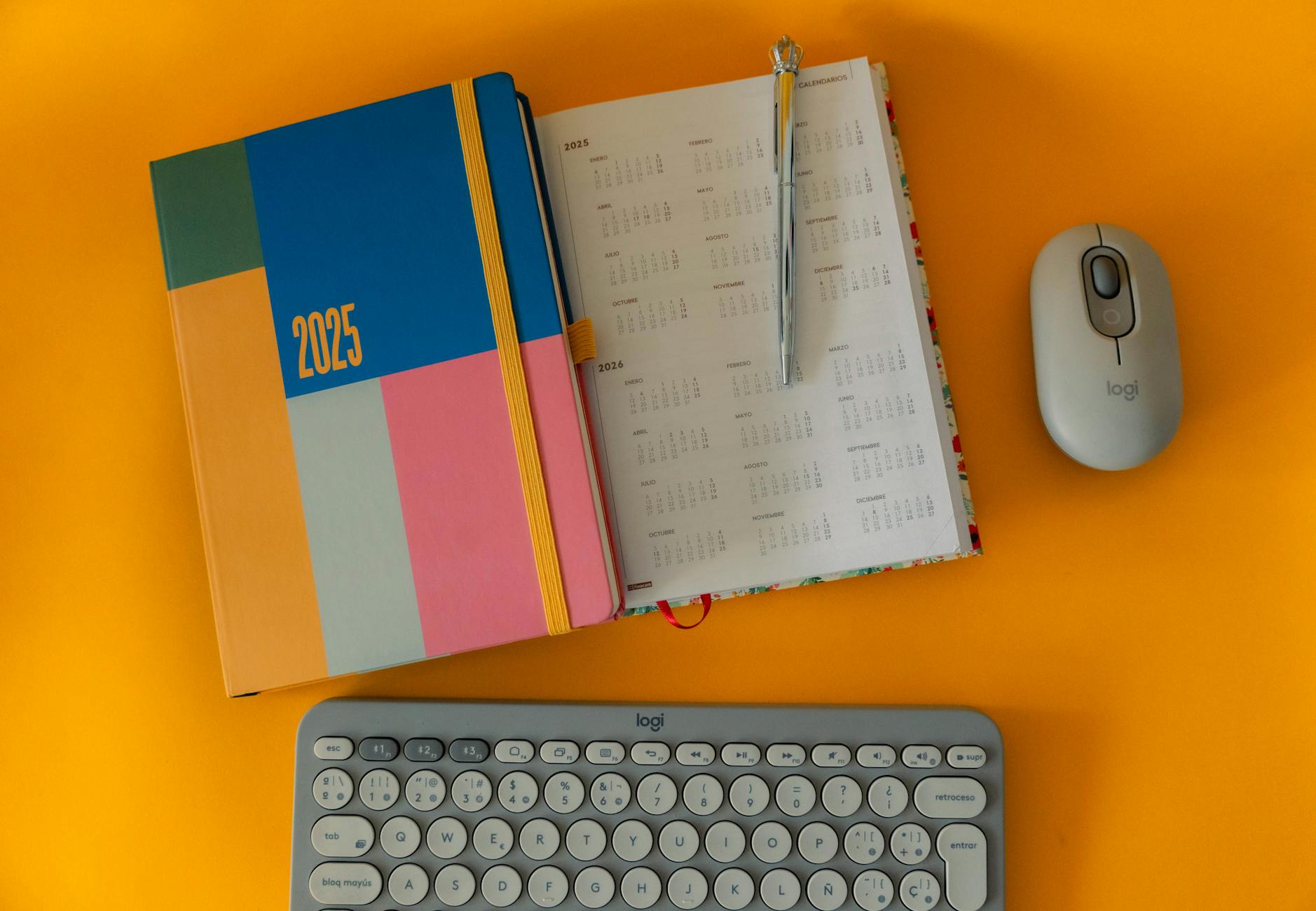 Vibrant 2025 planner with calendar, keyboard, and mouse on orange background.