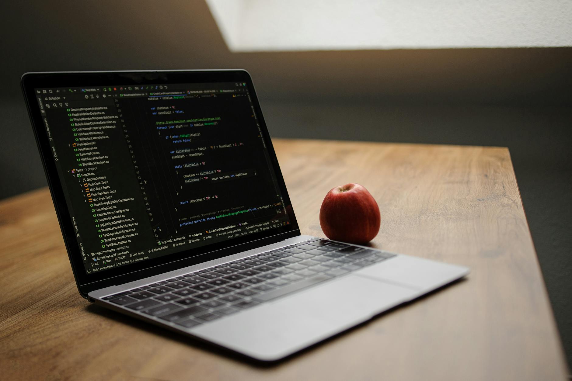 Open laptop displaying code next to a red apple on a wooden desk.